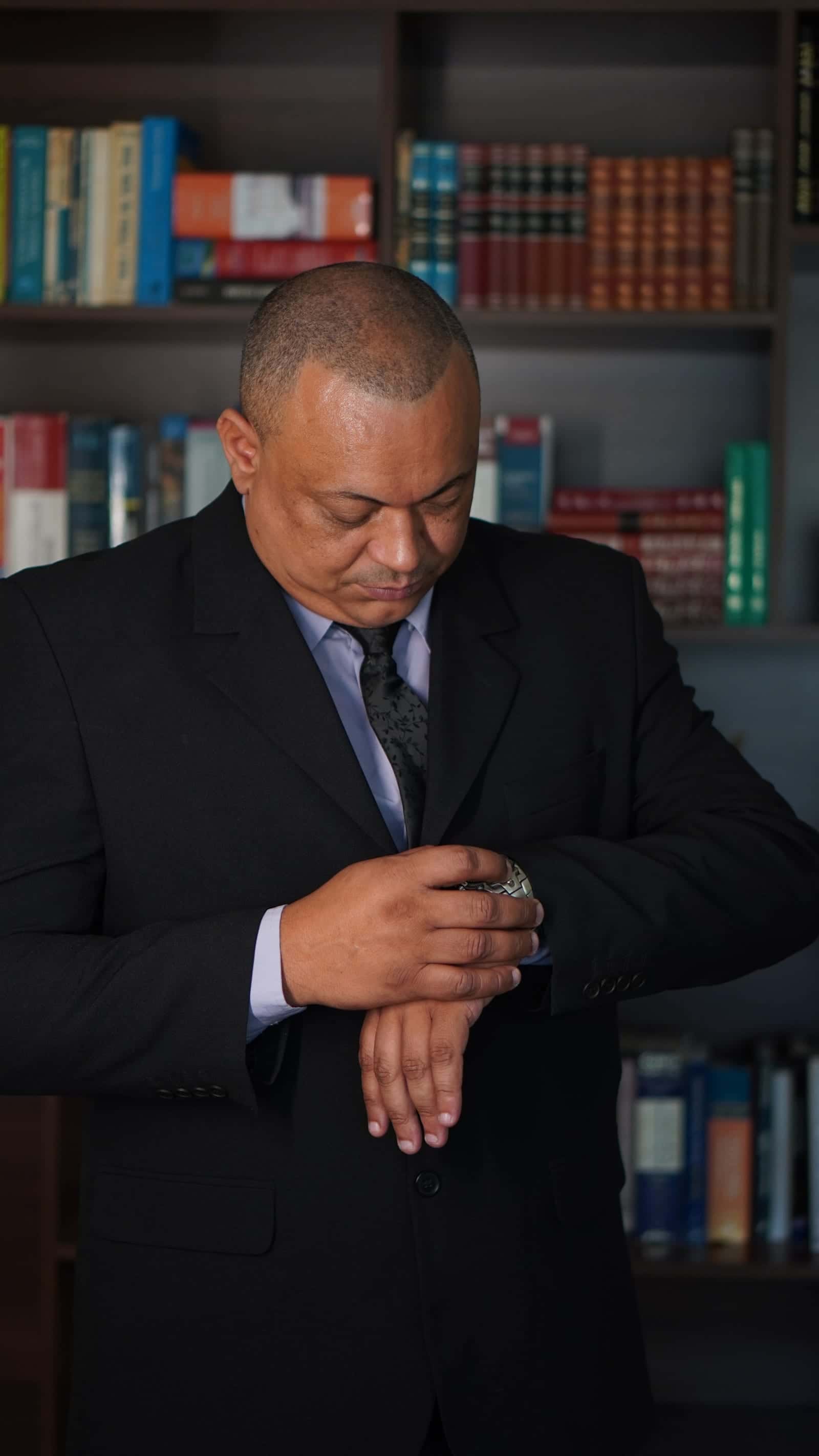 Dr. Edenilson Maria de Souza, advogado, conferindo o relógio de pulso diante de uma estante de livros
